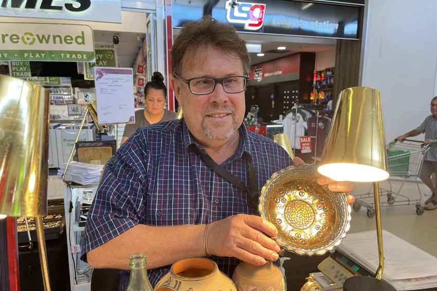 Cairns Antique Fair stallholder Richard MacDonald with a carnival glass bowl, Navajo Indian pots, pocket watches, a rare 1944 Coca Cola bottle and other items.