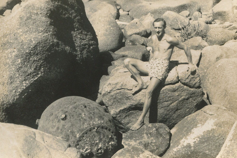 Conservationist John Büsst standing against rocks, looking down on what appears to be a WW2 sea mine on Bedarra Island. Picture: Virginia Edlington Collection