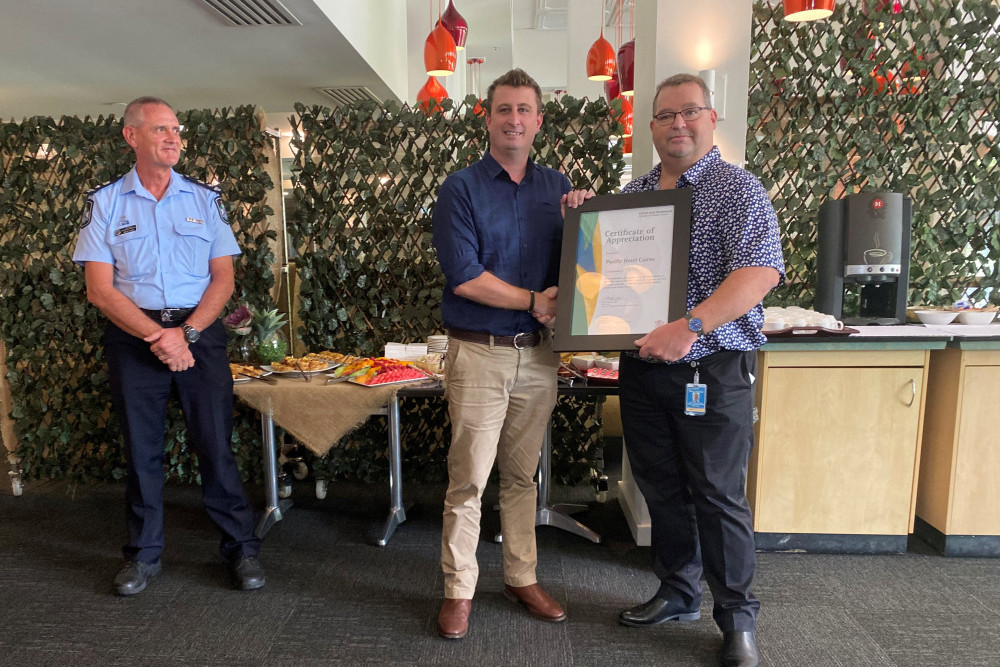 QPS Inspector Brad Winks looks on as Pacific Hotel General Manager Tim Moloney is presented with a certificate of thanks from CHHHS Acting Chief Executive Steve Thacker